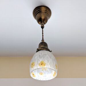 A hanging lamp with yellow flowers etched into the glass shade